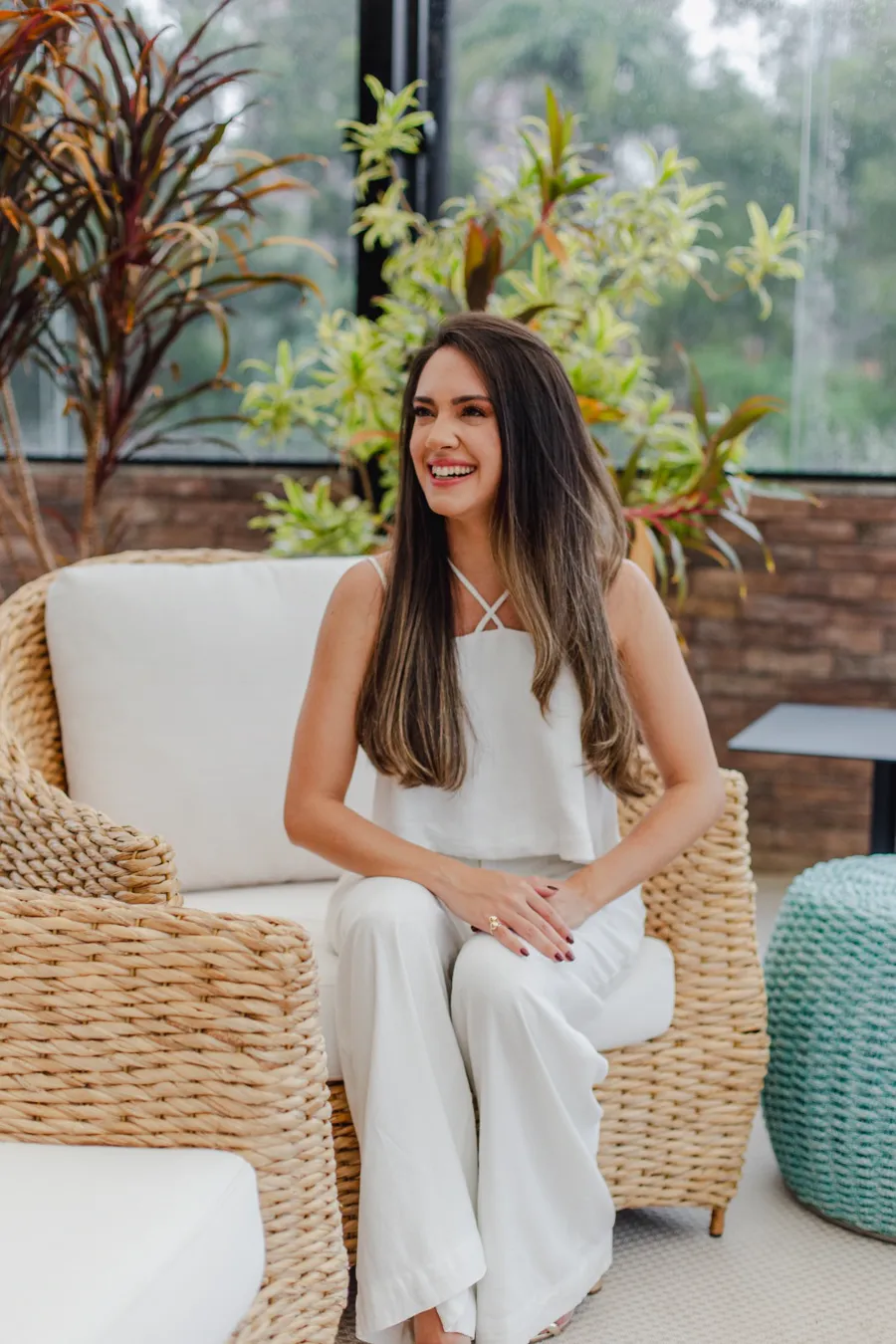 Jéssica Estrela sorrindo, sentada numa poltrona de fibra natural entre plantas